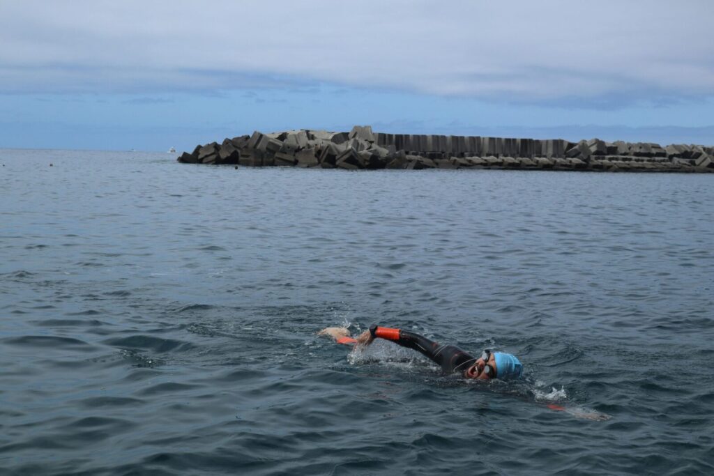 Man swimming in open sea near a coastal breakwater, showcasing recreational sport.
